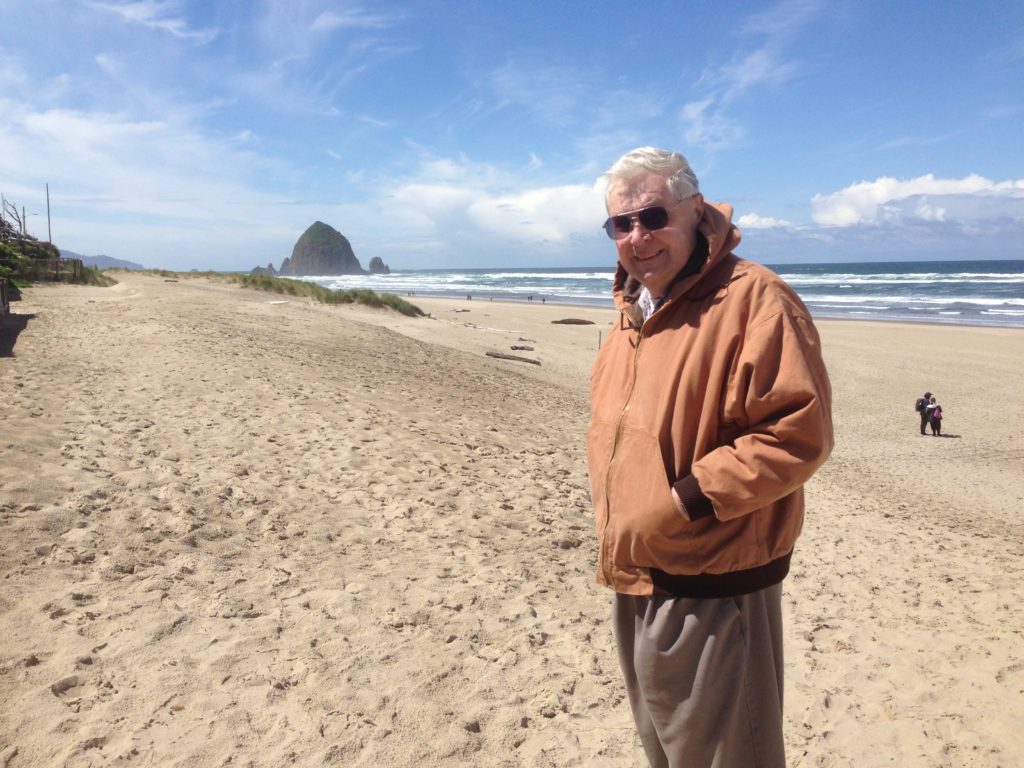 Photo of Doug, standing on a beach near Haystack Rock, Cannon Beach, Oregon.